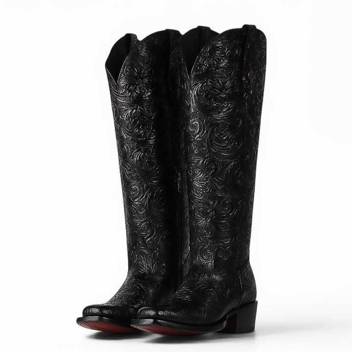 A pair of black leather cowboy boots with intricate floral tooling on the shafts, shown from a three-quarter angle against a plain white background.