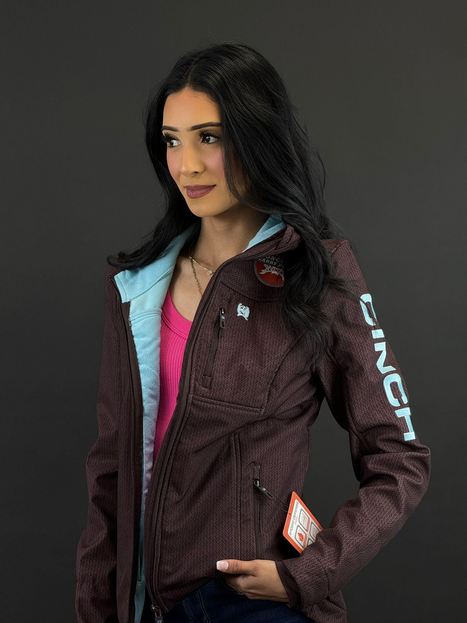 Cinch Softshell marrón para mujer con logotipo azul en la manga y cremallera completa, bolsillo de transporte oculto