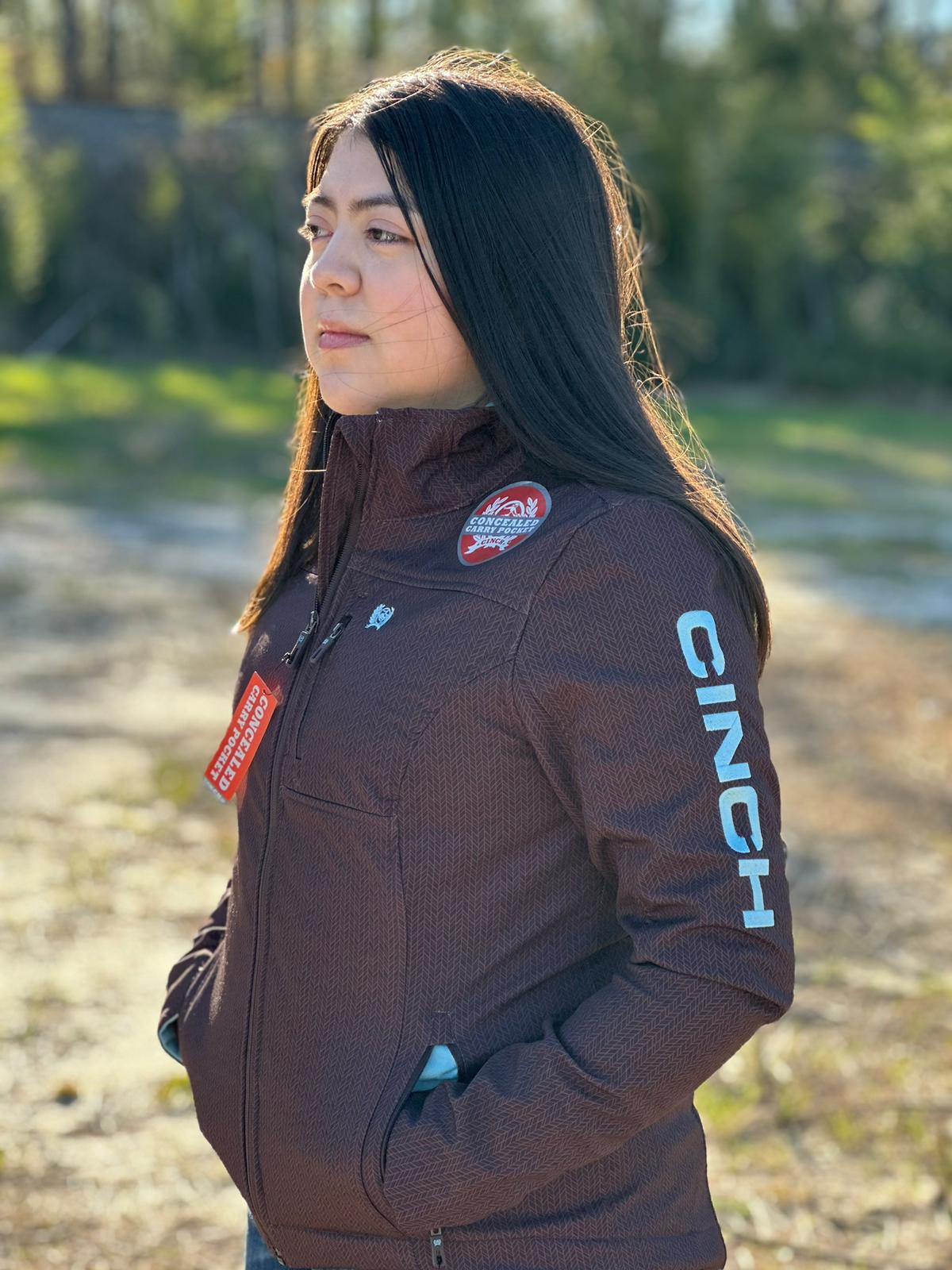 Cinch Softshell marrón para mujer con logotipo azul en la manga y cremallera completa, bolsillo de transporte oculto